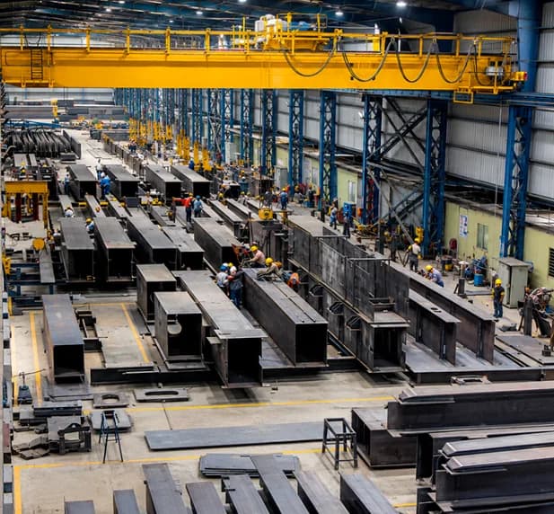 Fabrication shop floor with built-up steel beams under a yellow overhead crane